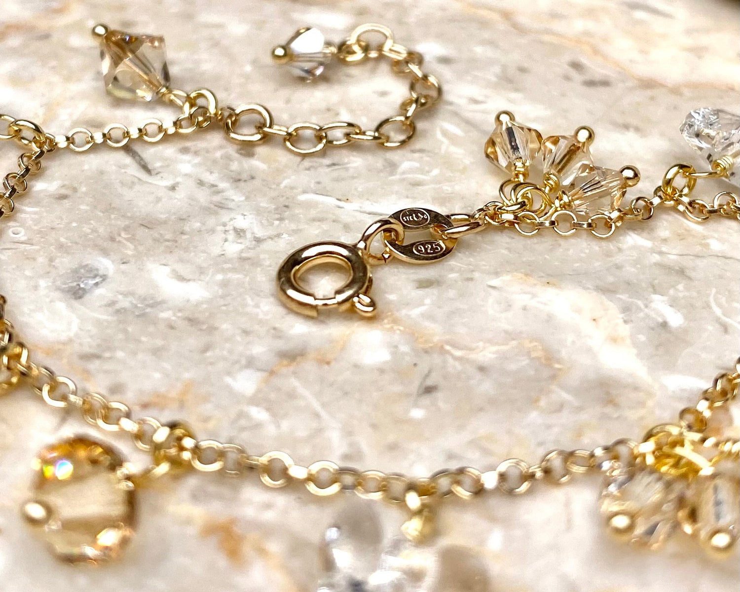 Lähikuva kultaisesta rannekorusta, jossa on beigejä kristalleja