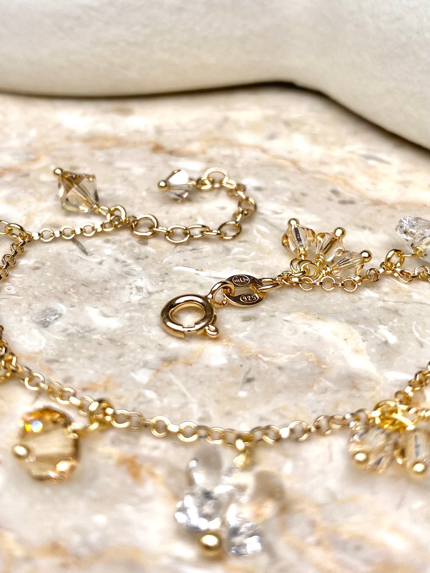 Lähikuva kultaisesta rannekorusta beigeillä kristalleilla