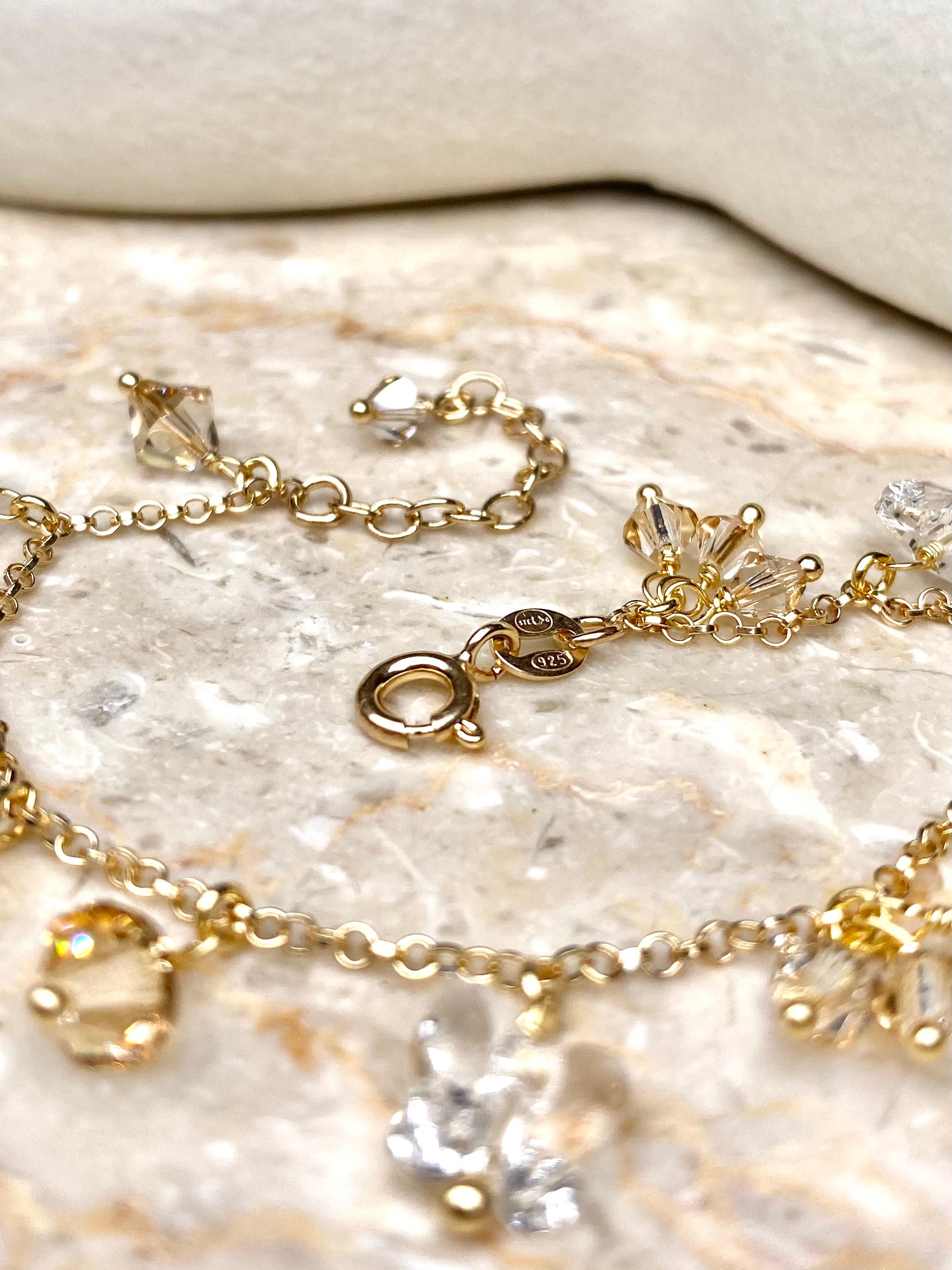 Lähikuva kultaisesta rannekorusta beigeillä kristalleilla