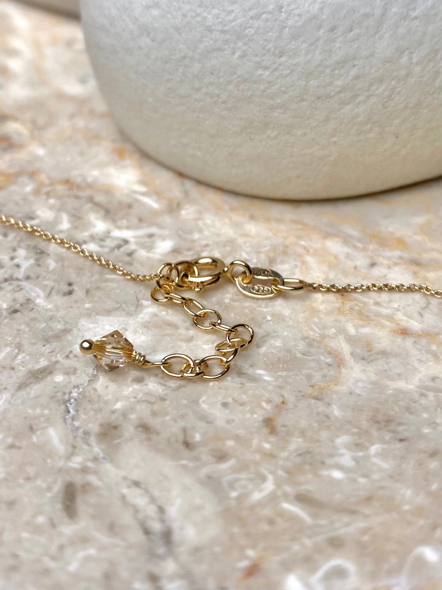 Kultainen kaulakorun lukko, jossa on kiinni yksi beige kristallihelmi