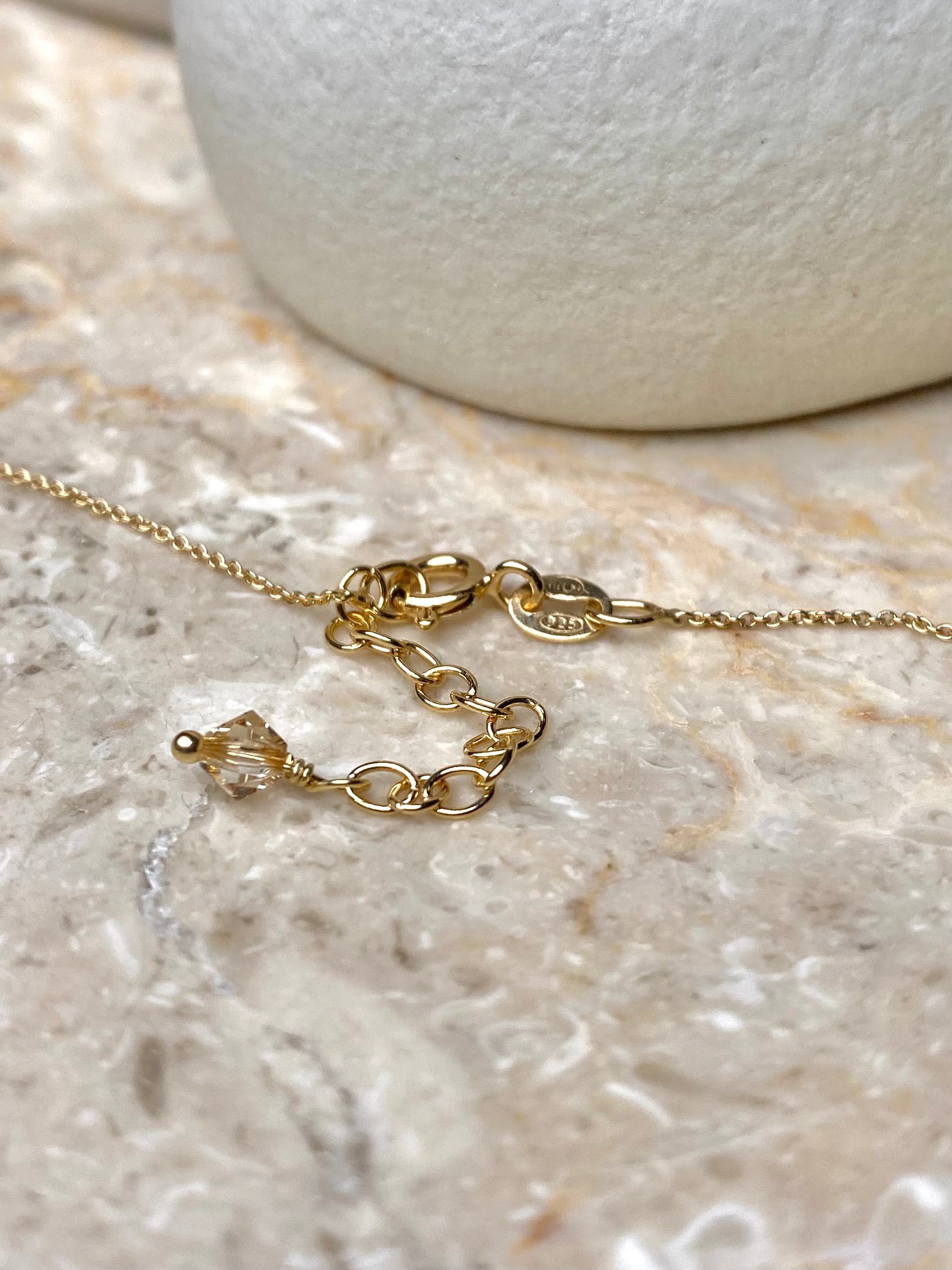 Kultainen kaulakorun lukko, jossa on kiinni yksi beige kristallihelmi