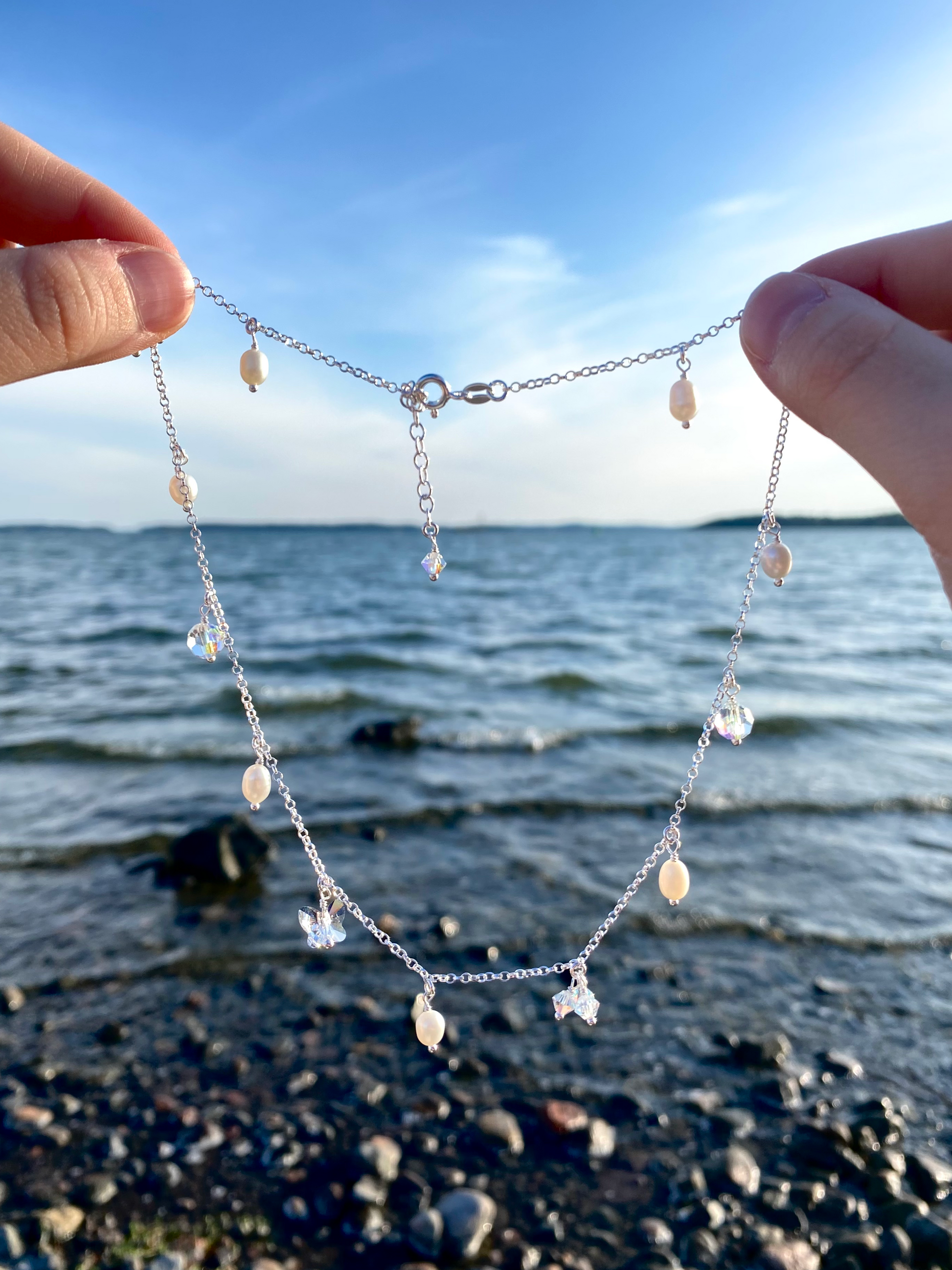 Hopeinen kaulakoru, jossa pieniä kristalli- ja helmiriipuksia