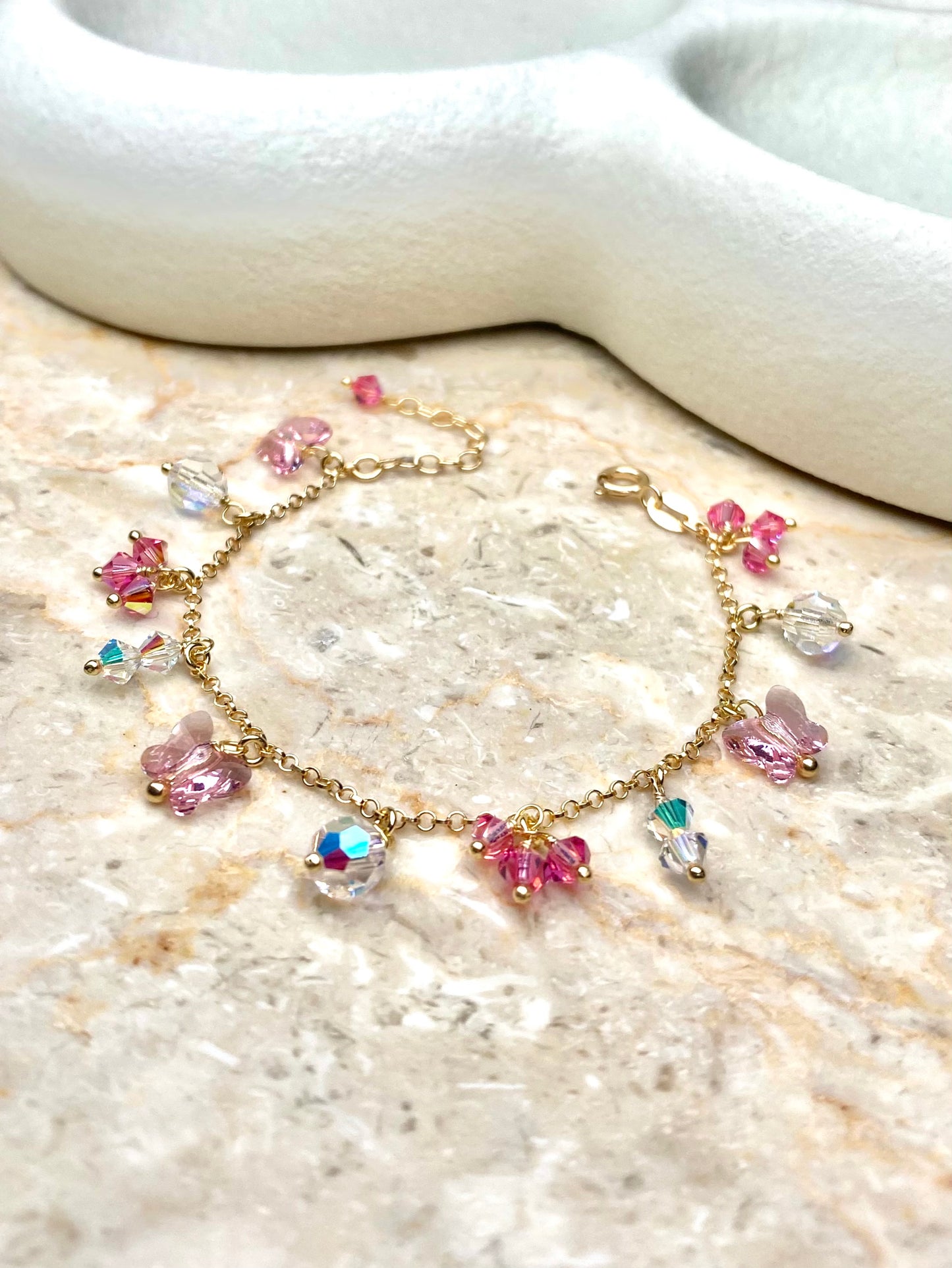 Kullattu hopeinen vaaleanpunainen rannekoru, jossa on pieniä riipuksia koristeena