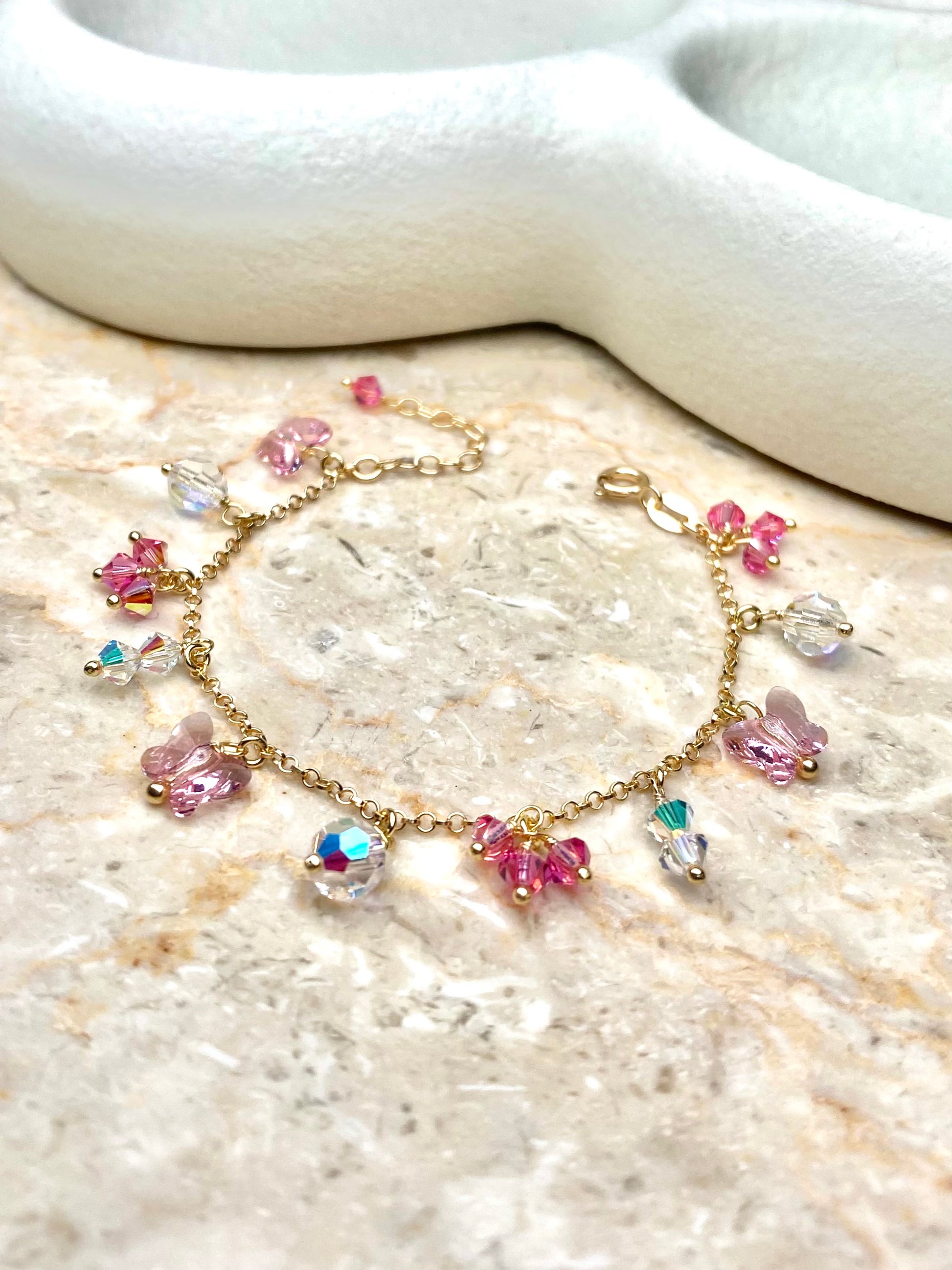 Kullattu hopeinen vaaleanpunainen rannekoru, jossa on pieniä riipuksia koristeena