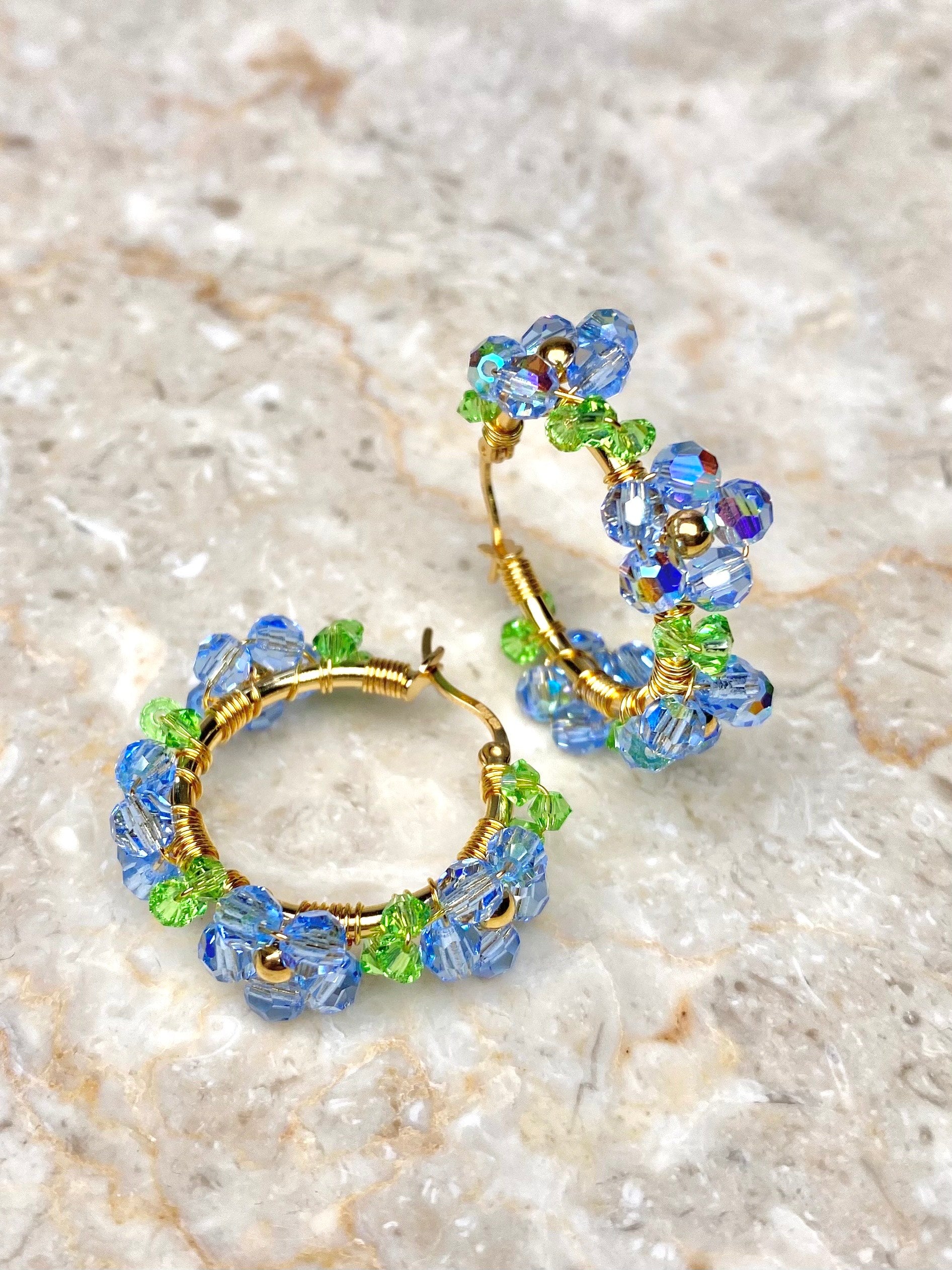 Kultaiset rengaskorvakorut, koristeltu vaaleansinisillä kukilla.