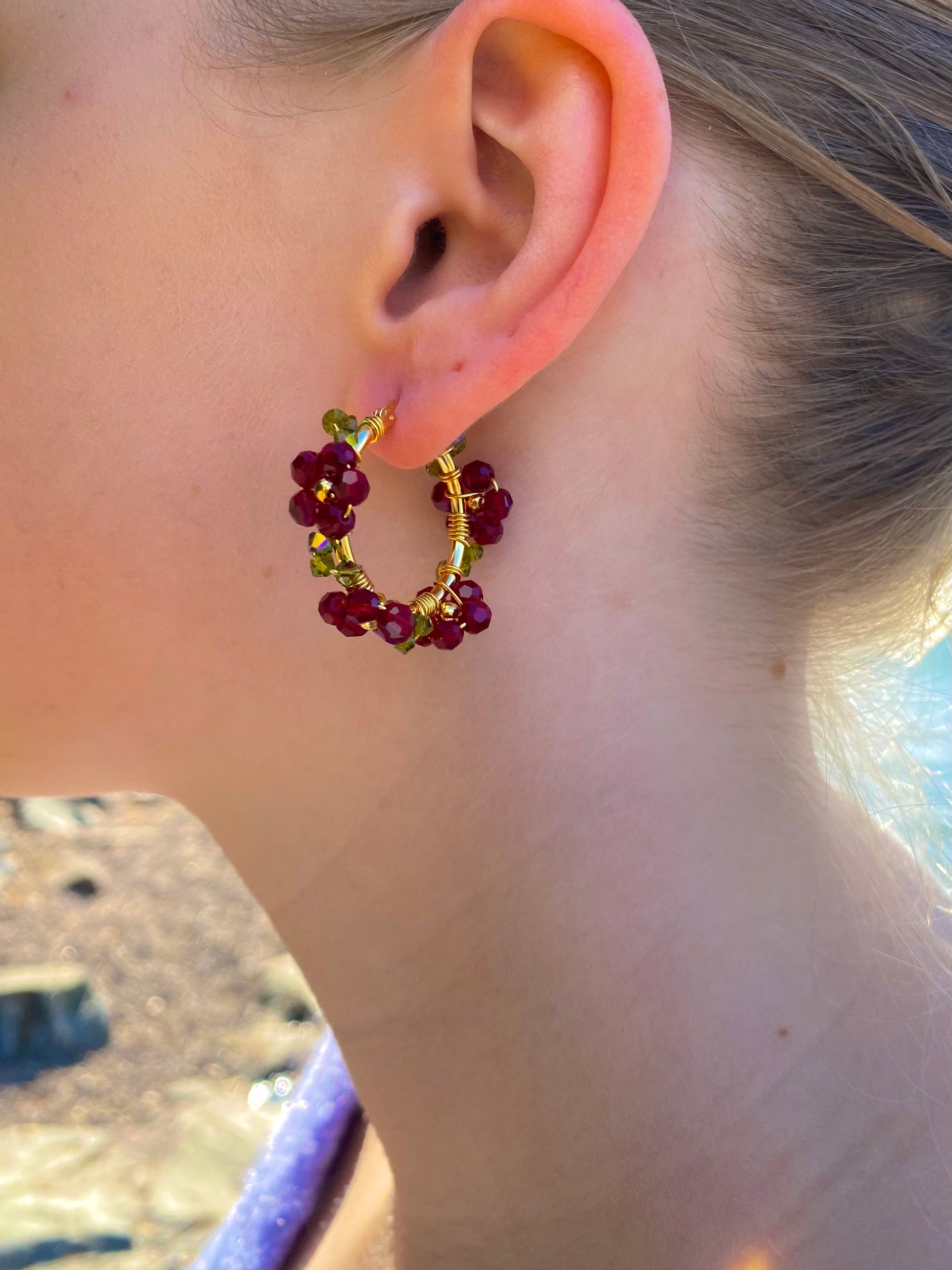 Kultaiset tummanpunaiset kukkakorvakorut mallin korvassa