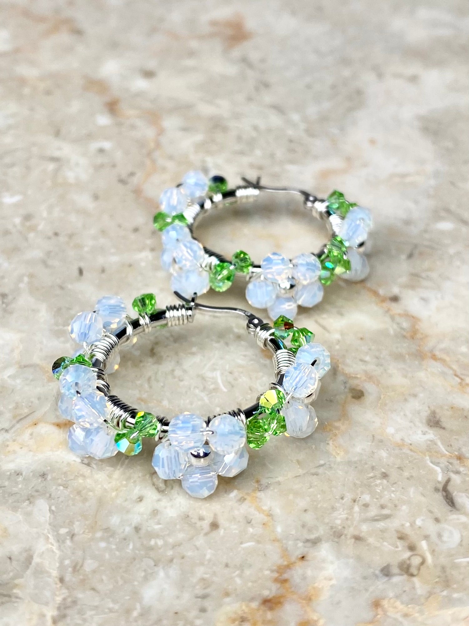 Lähikuva valkoisista hopeisista rengaskorvakoruista, koristeltu kukilla.