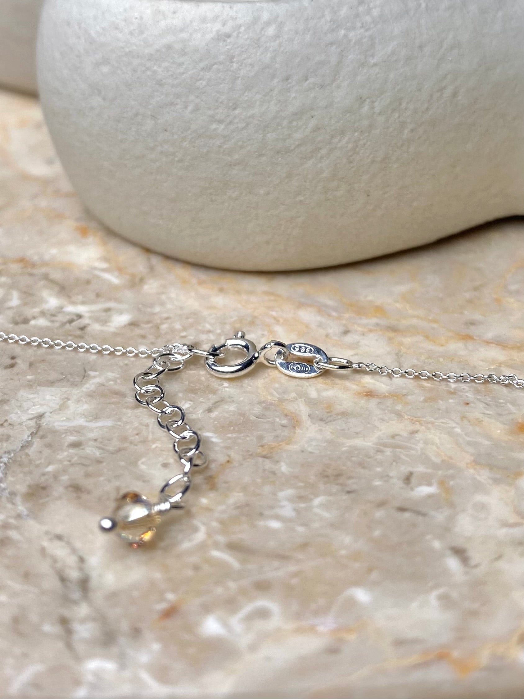 Lähikuva hopeisesta sirosta kaulakorusta, jossa on beigejä kristalleja.