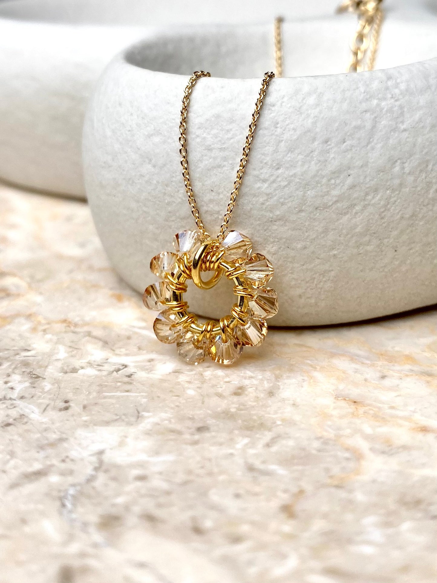 Lähikuva kaulakoruriipuksesta, joka on renkaan muotoinen ja siinä on beigejä kristalleja.