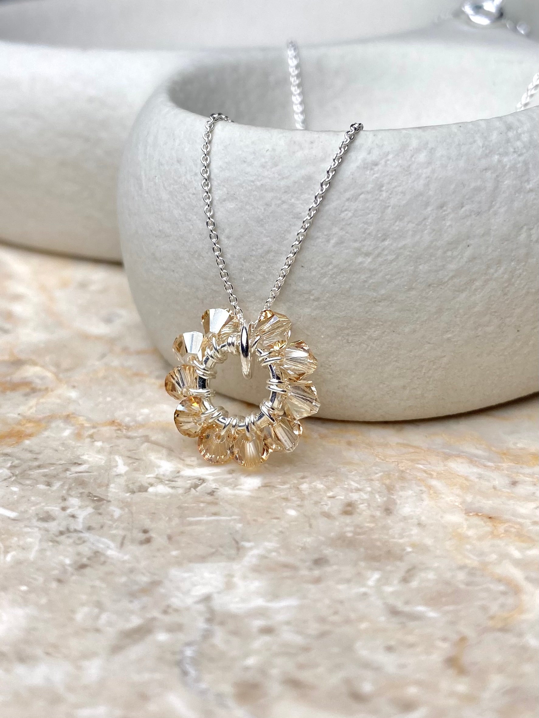 Hopeinen kaulakoru pienellä rengasriipuksella, jossa on beigejä kristalleja.