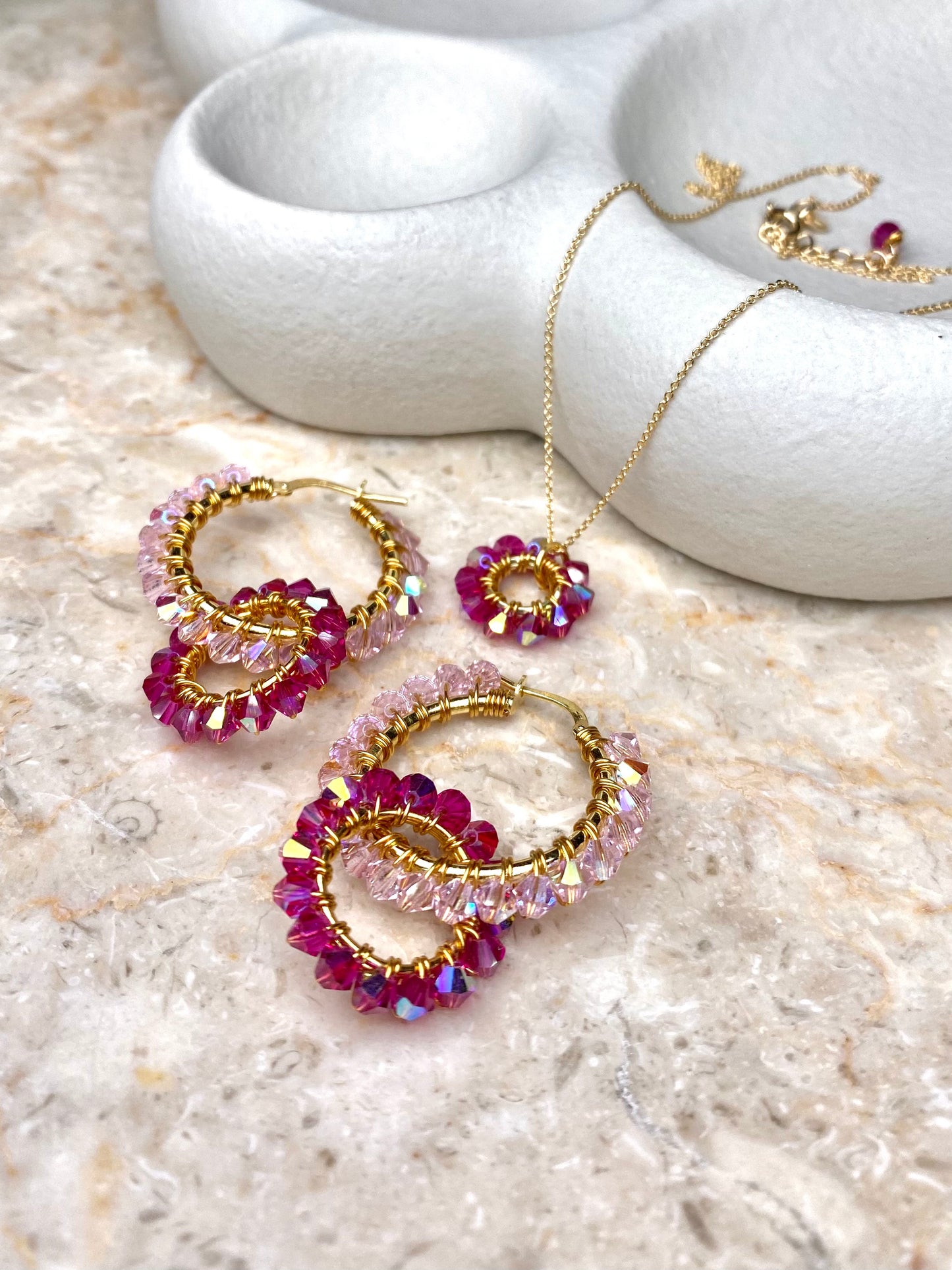 Värikäs kultainen korusetti, jossa vaaleanpunaisia kristalleja korvakoruissa ja kaulakorussa